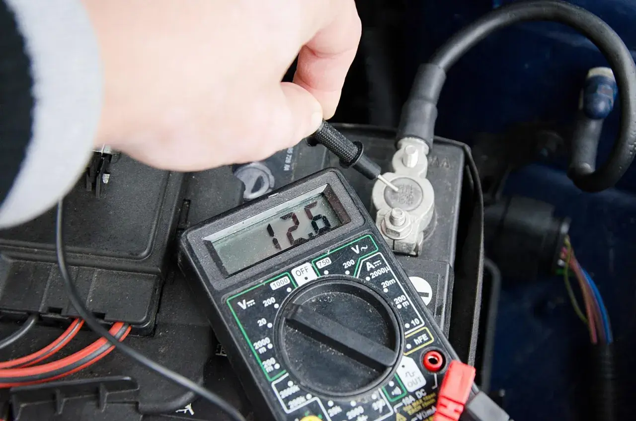 Sprawdzanie prawidłowego napięcia akumulatora multimetrem. Wynik 12.6V wskazuje na dobry stan.